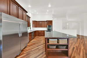 Kitchen featuring an expansive center island with countertop seating, rich wood cabinetry, stainless steel appliances, modern recessed lighting, and wood-finish flooring