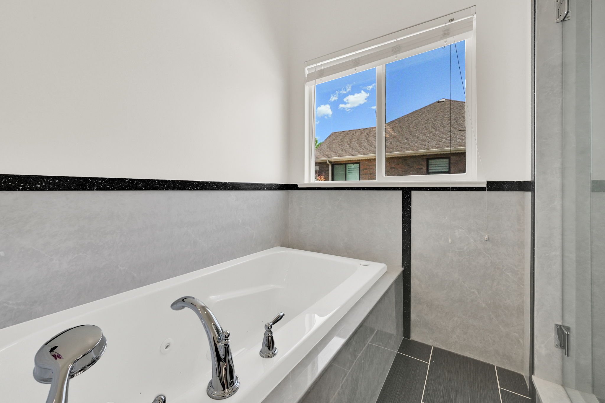 Soaking tub featuring chrome fixtures, light-toned wall tile, and black accent trim