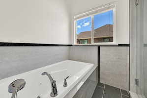 Soaking tub featuring chrome fixtures, light-toned wall tile, and black accent trim