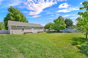 Expansive green lawn featuring a detached accessory building with board and batten siding, multiple windows, and a shingled roof