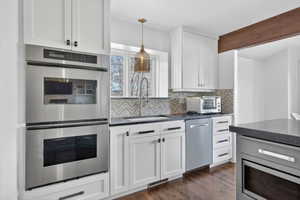 Kitchen featuring white shaker cabinetry, stainless steel double wall ovens, a herringbone-patterned tile backsplash, dark countertops, and wood-finish flooring