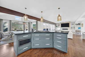 Open-concept kitchen featuring a multi-sided island with under-counter microwave and gas cooktop, dark countertops, and pendant lighting