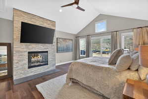 Vaulted ceilings with a ceiling fan, a stone-faced fireplace with a hearth, wood-finish flooring, and multiple windows with mountain scenery