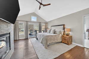 Vaulted ceiling bedroom featuring wood-finish flooring and a stone-clad fireplace