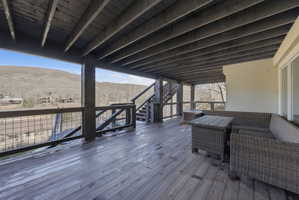 Expansive wood-finish deck with a mountain backdrop, featuring a covered ceiling, integrated staircase, and durable metal railing