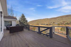 Expansive outdoor deck featuring wood-finish flooring, a sturdy railing with metal infill, and a broad mountain backdrop