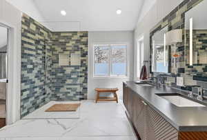 Spacious bathroom featuring a glass-enclosed shower with subway tile, dual vanity with undermount sinks, and white marble-look flooring