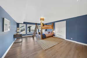 Spacious room featuring wood-finish flooring, two large windows, a built-in closet with bi-fold doors, and a sloped ceiling