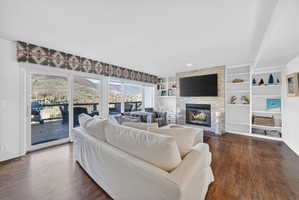 Spacious living area featuring wood-finish flooring, a stone-faced fireplace, and built-in shelving
