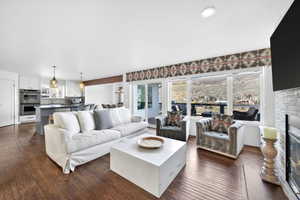Open-concept living space featuring wood-finish flooring, a stone-clad fireplace, and expansive windows