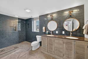 Expansive bathroom featuring a dual vanity with louvered cabinetry, an integrated shower with dark subway tile, and wood-finish flooring with a geometric pattern