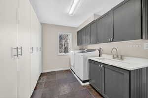 Dedicated utility space featuring extensive white cabinetry, dark slate flooring, a window providing natural light, and a built-in sink with dark gray base and upper cabinetry