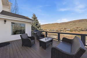 Expansive outdoor deck featuring wood-finish flooring, a contemporary metal railing, and a hillside backdrop