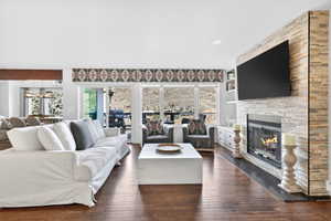 Living area featuring wood-finish flooring, a stone-clad fireplace with a glass-front insert, built-in shelving, and large sliding glass doors opening to an outdoor deck