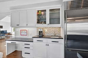 Integrated wet bar area featuring white shaker cabinetry, black countertops, a decorative tile backsplash, and a built-in stainless steel refrigerator