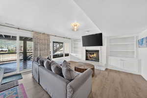 Living area featuring a white brick fireplace, built-in shelving, wood-finish flooring, and a sliding glass door opening to an outdoor deck