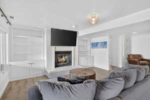 Living area featuring a white brick fireplace with hearth, integrated television mount, and built-in shelving with lower cabinetry
