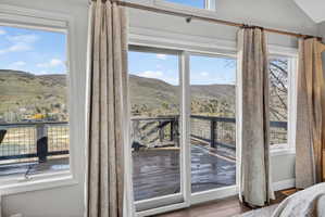 Sliding glass door opening onto an outdoor deck with metal railing, bordered by multiple windows with patterned drapes
