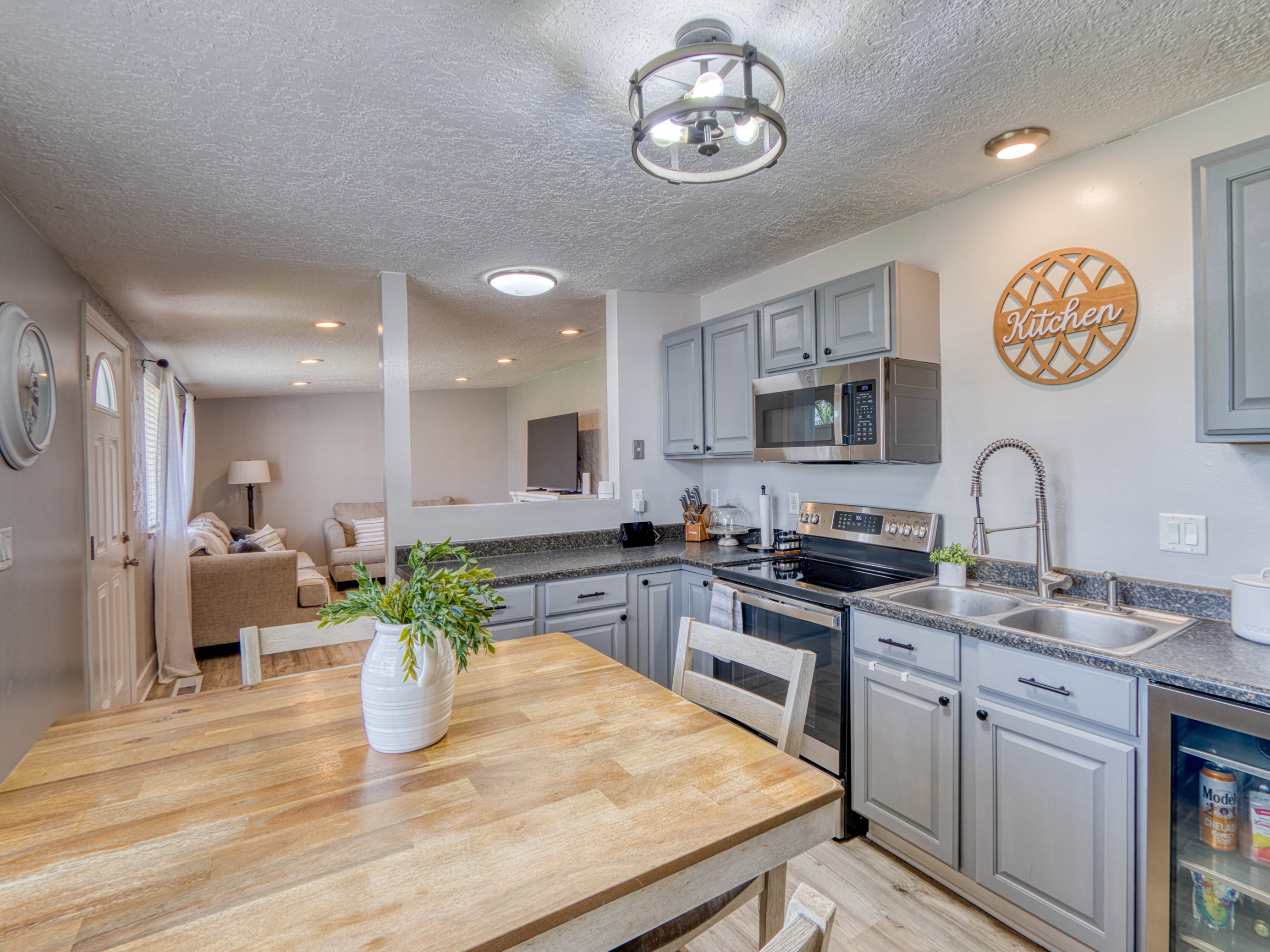 Modern kitchen featuring light gray cabinetry, dark speckled countertops, stainless steel appliances, a double basin sink, and recessed lighting
