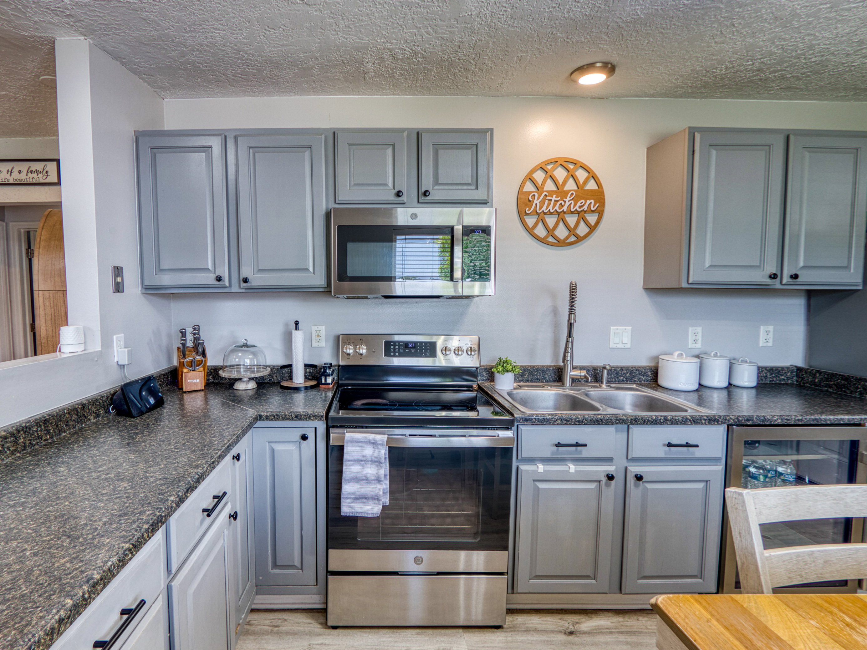 Kitchen featuring gray cabinetry with black hardware, dark speckled countertops, and stainless steel appliances including a range, microwave, and beverage cooler