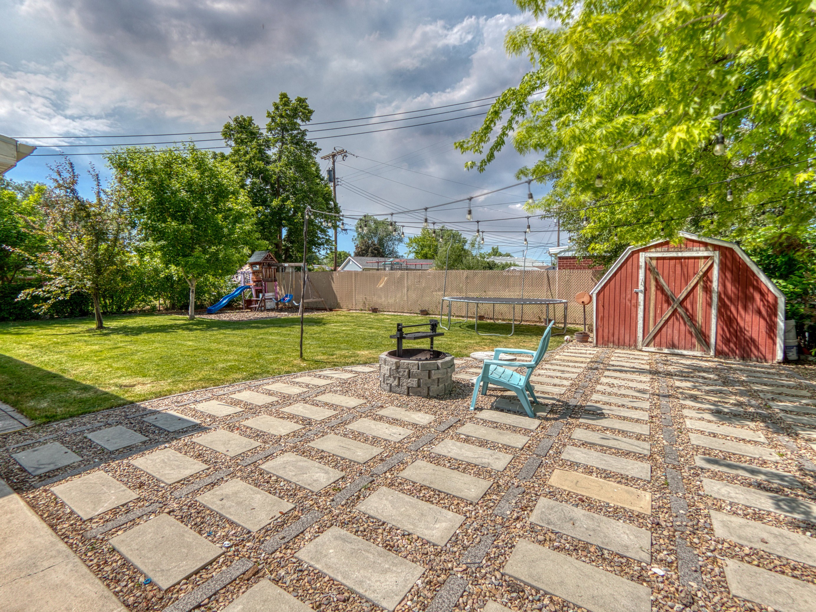 Expansive backyard featuring a stone paver patio with gravel fill, a built-in stone fire pit, a red barn-style shed, and mature trees