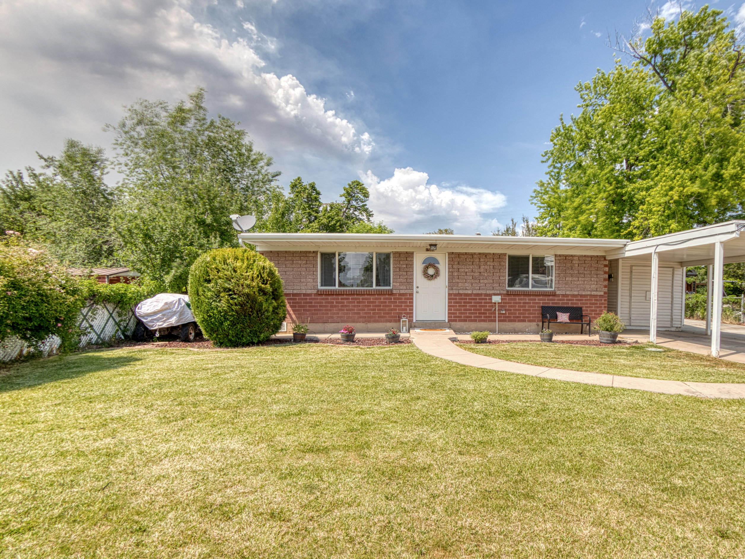 Brick exterior with a white entry door, front yard lawn, concrete walkway, and an attached carport
