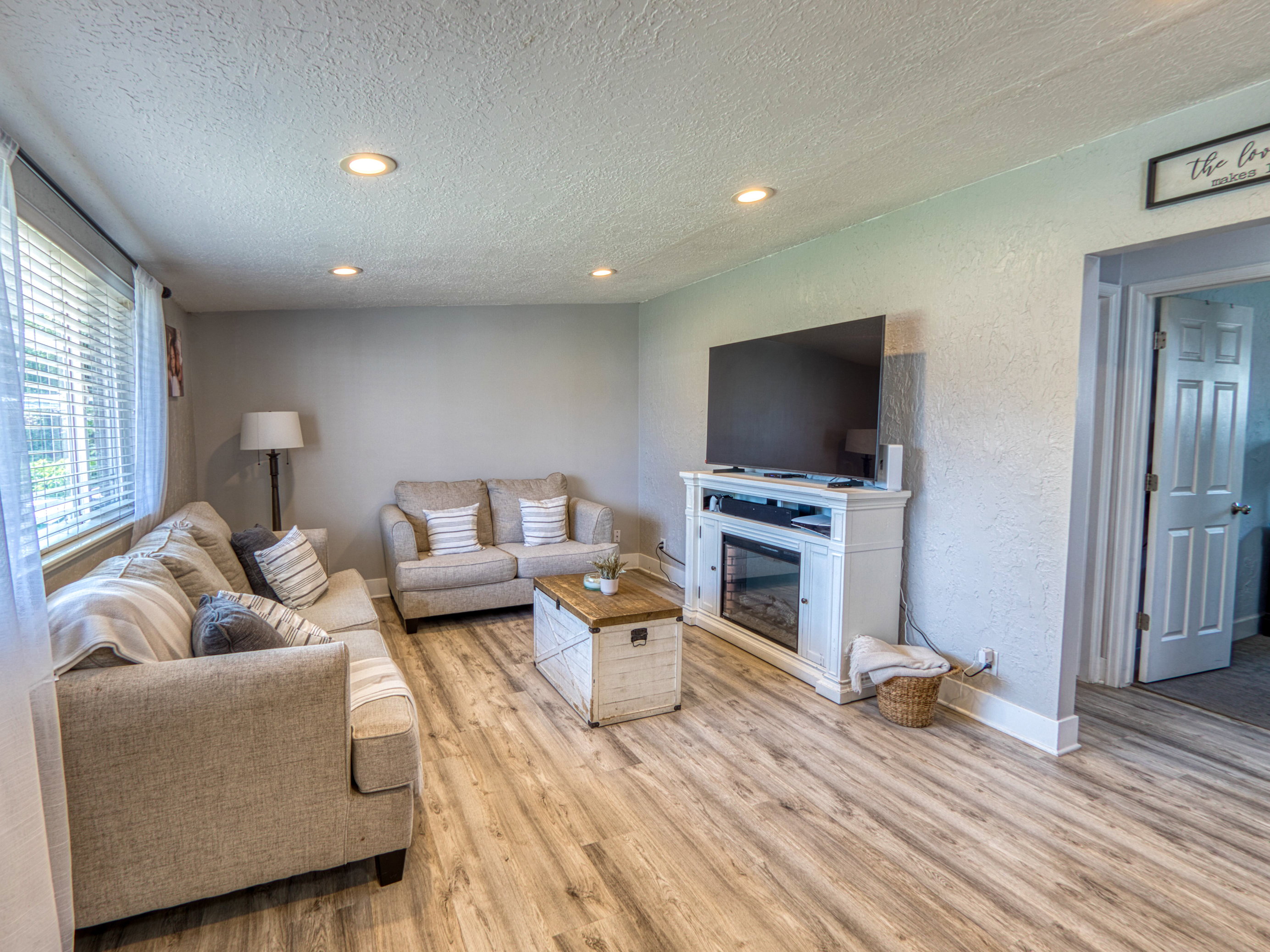 Living room featuring recessed ceiling lighting, light wood-finish flooring, a white mantel with an electric fireplace insert, and baseboard molding