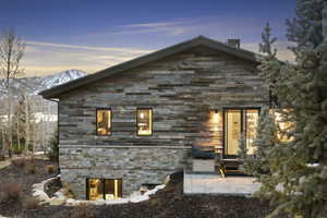 Exterior featuring horizontal wood siding, natural stone veneer, a sloped roofline, a ground-level patio with pavers, and a prominent mountain backdrop