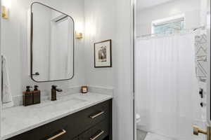 Modern bathroom featuring a dark wood-finish vanity with brass hardware, a white countertop with an integrated sink, a rectangular framed mirror, and wall-mounted sconces