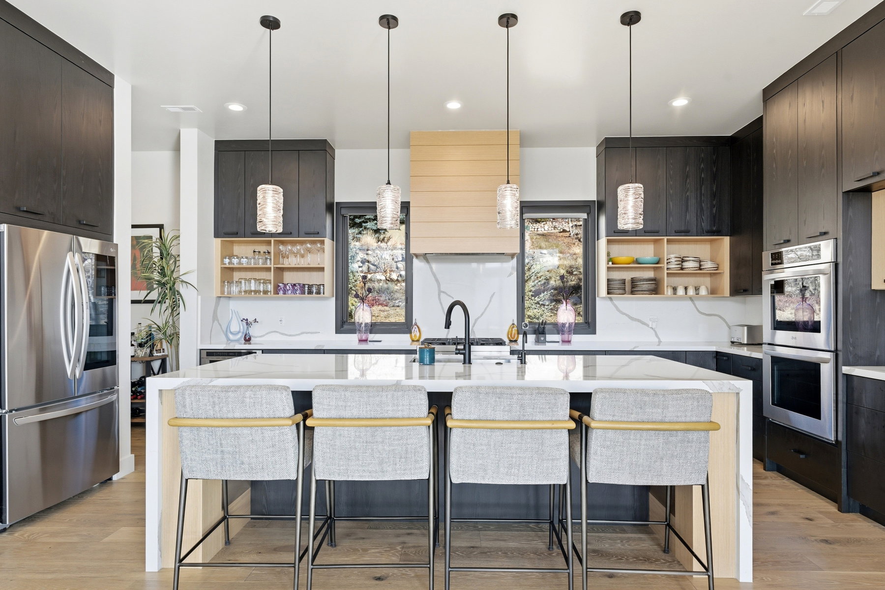 Gourmet kitchen featuring a waterfall island with integrated seating, stone countertops with a dramatic veining pattern, dark wood-finish cabinetry, stainless steel appliances, and a light wood-finish range hood