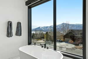 Freestanding soaking tub with matte black fixtures, set against a large window framing a mountain and lake landscape