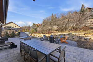 Expansive paver patio with a built-in hot tub, stone retaining wall, and a fire pit area