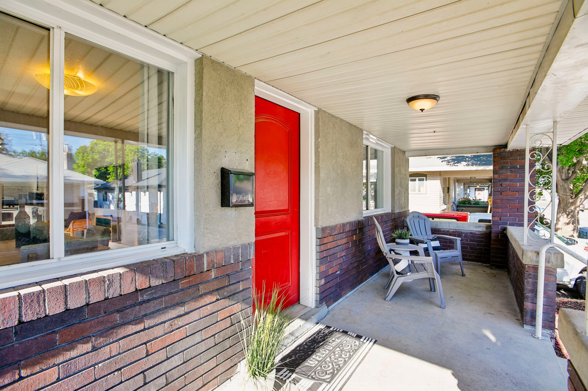 Inviting covered front porch featuring a vibrant red entry door, white window trim, brick accents, and a stucco exterior finish