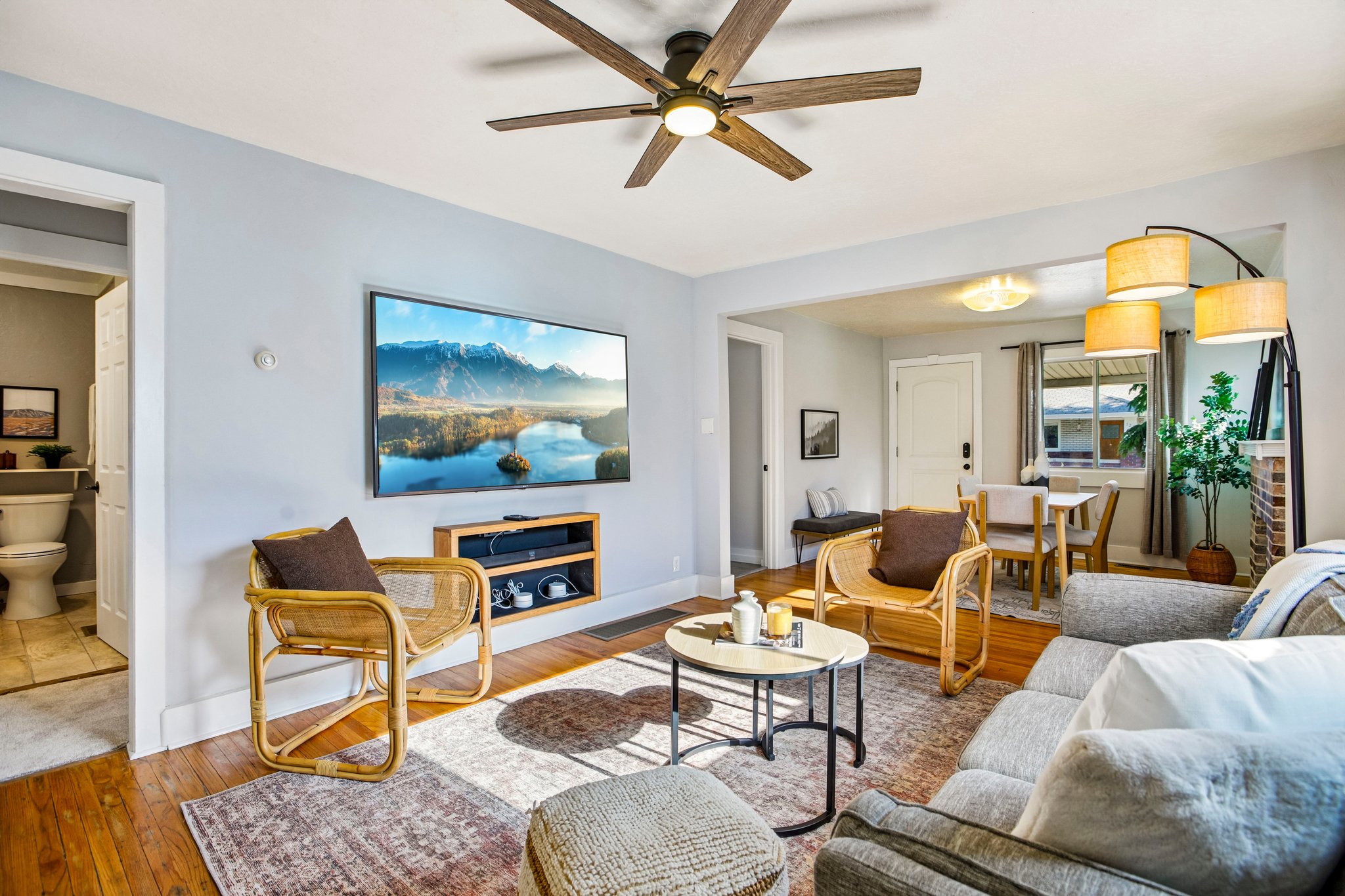 Living area featuring wood-finish flooring, a ceiling fan with integrated lighting, and a wall-mounted media console