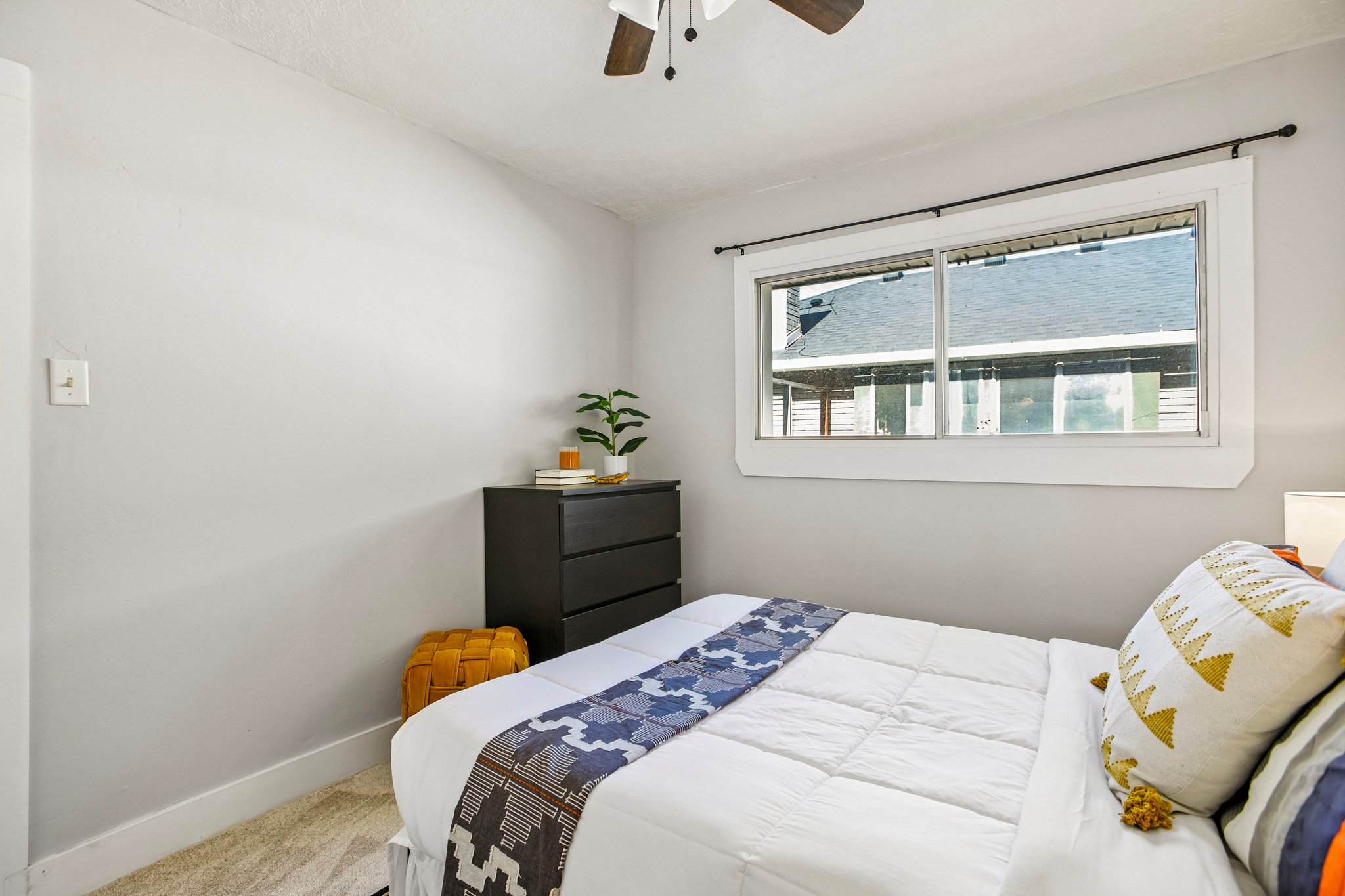 Bright room featuring light grey walls, white trim, a large window with a black curtain rod, and a ceiling fan with wood-finish blades