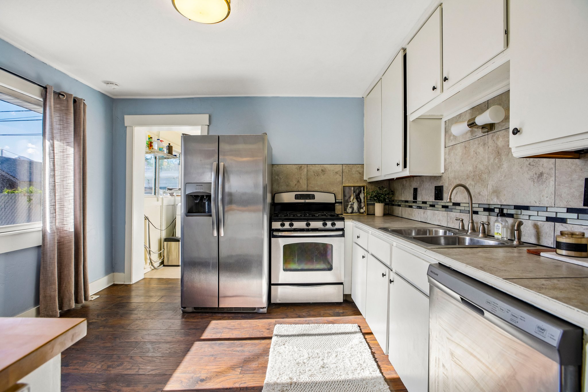 Kitchen featuring stainless steel appliances, white cabinetry, dark wood-finish flooring, and a tiled backsplash with decorative accents