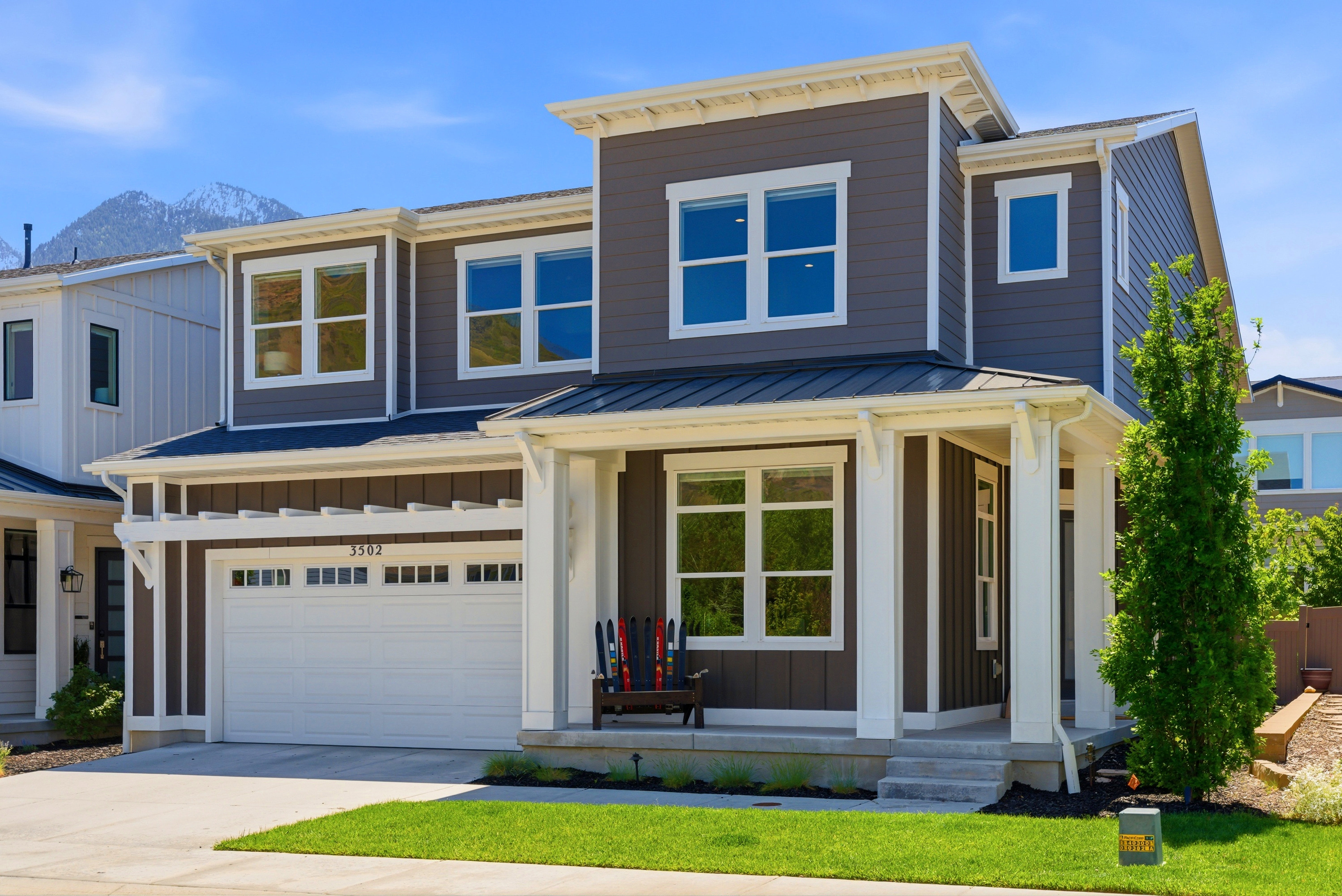 Contemporary two-story residence featuring dark siding with white trim accents, a covered front porch, an attached garage with upper transom windows, multiple large windows, and a prominent mountain backdrop