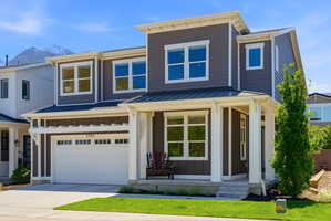 Contemporary two-story residence featuring dark siding with white trim accents, a covered front porch, an attached garage with upper transom windows, multiple large windows, and a prominent mountain backdrop