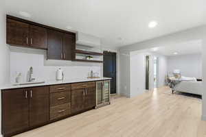 Wet bar featuring dark wood cabinetry, white countertops, stainless steel sink, and built-in beverage refrigerator