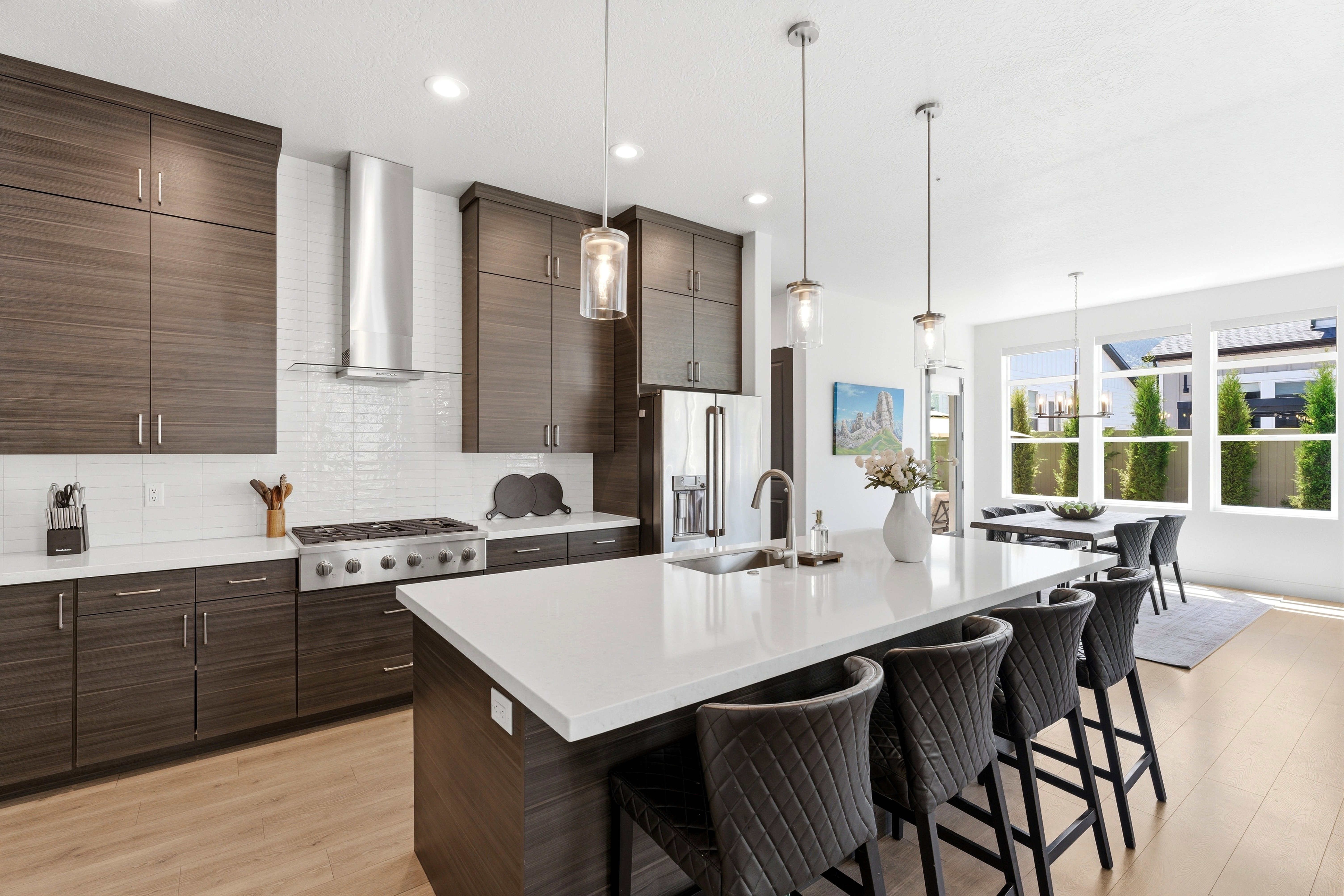 Modern kitchen featuring a large center island with seating, a stainless steel gas range with a matching range hood, and LVP-finish cabinetry