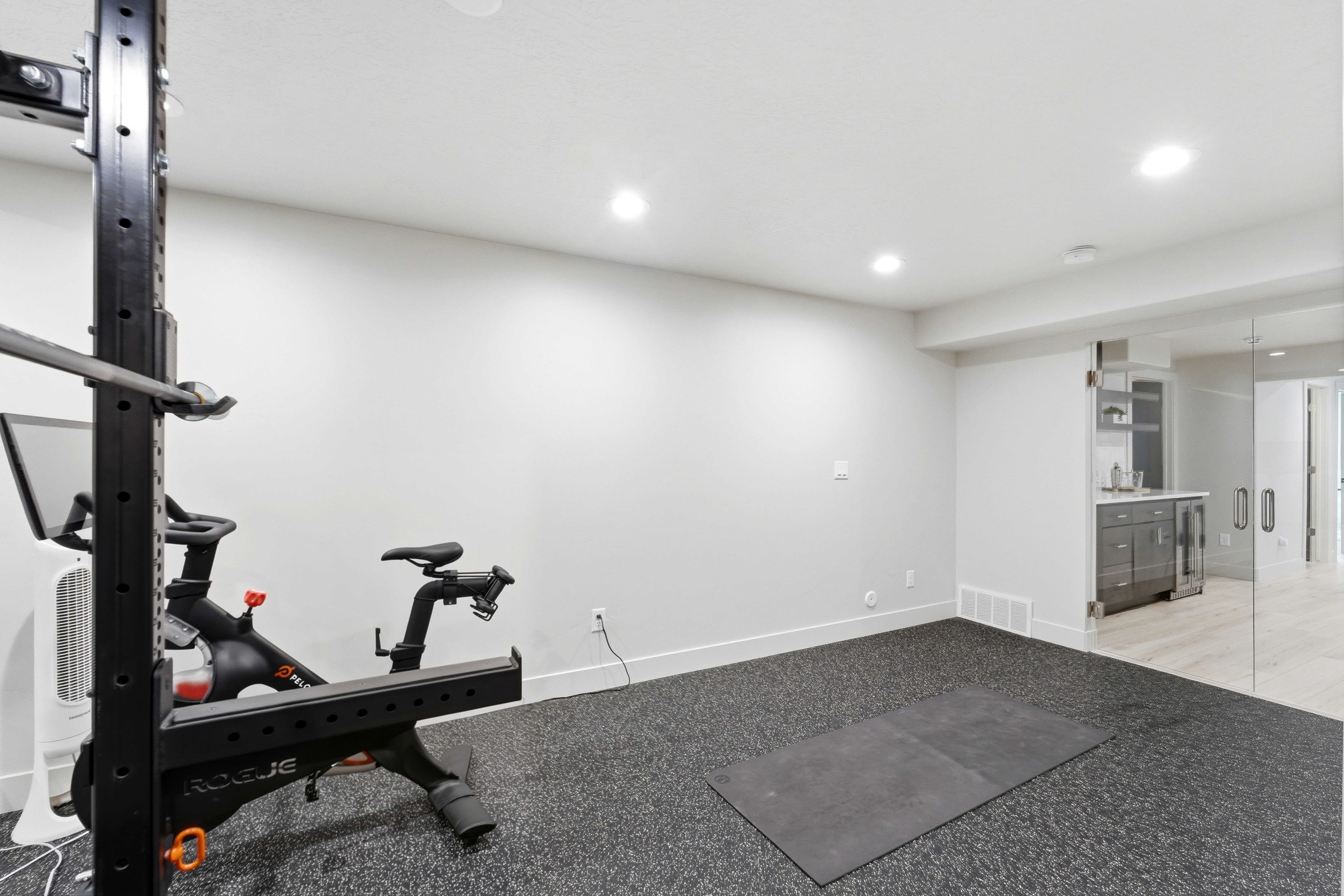 Dedicated fitness area featuring durable rubber flooring, recessed lighting, and a built-in wet bar with cabinetry and beverage refrigerator