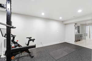 Dedicated fitness area featuring durable rubber flooring, recessed lighting, and a built-in wet bar with cabinetry and beverage refrigerator