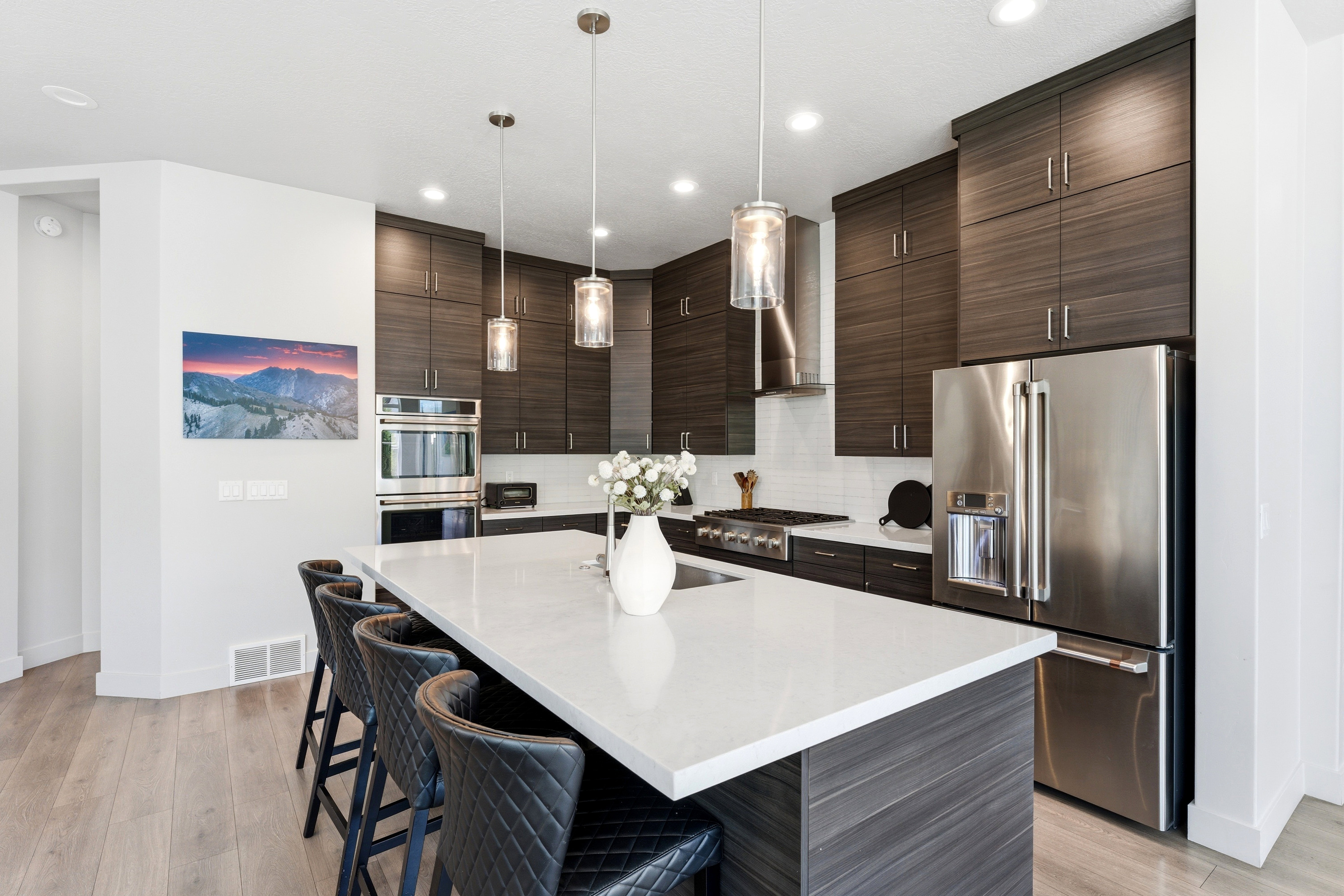 Modern kitchen featuring a large white countertop island, dark wood-finish cabinetry, stainless steel appliances, and wood-finish flooring