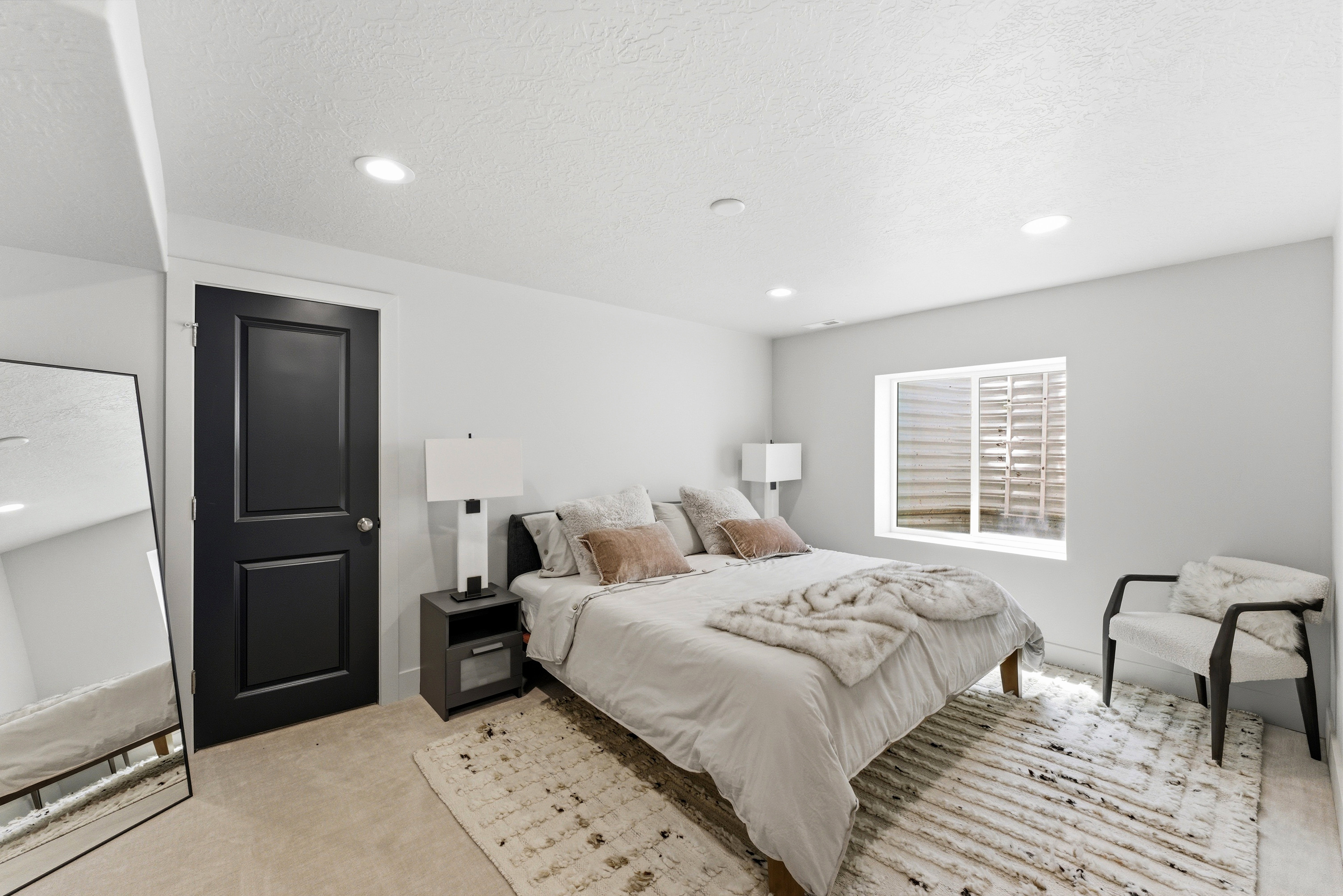 Recessed lighting illuminates a space featuring a contrasting black paneled door, a single egress window, and light-colored carpeting