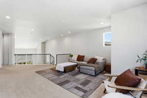 Open loft space featuring light-colored carpeting throughout, white walls, and recessed lighting