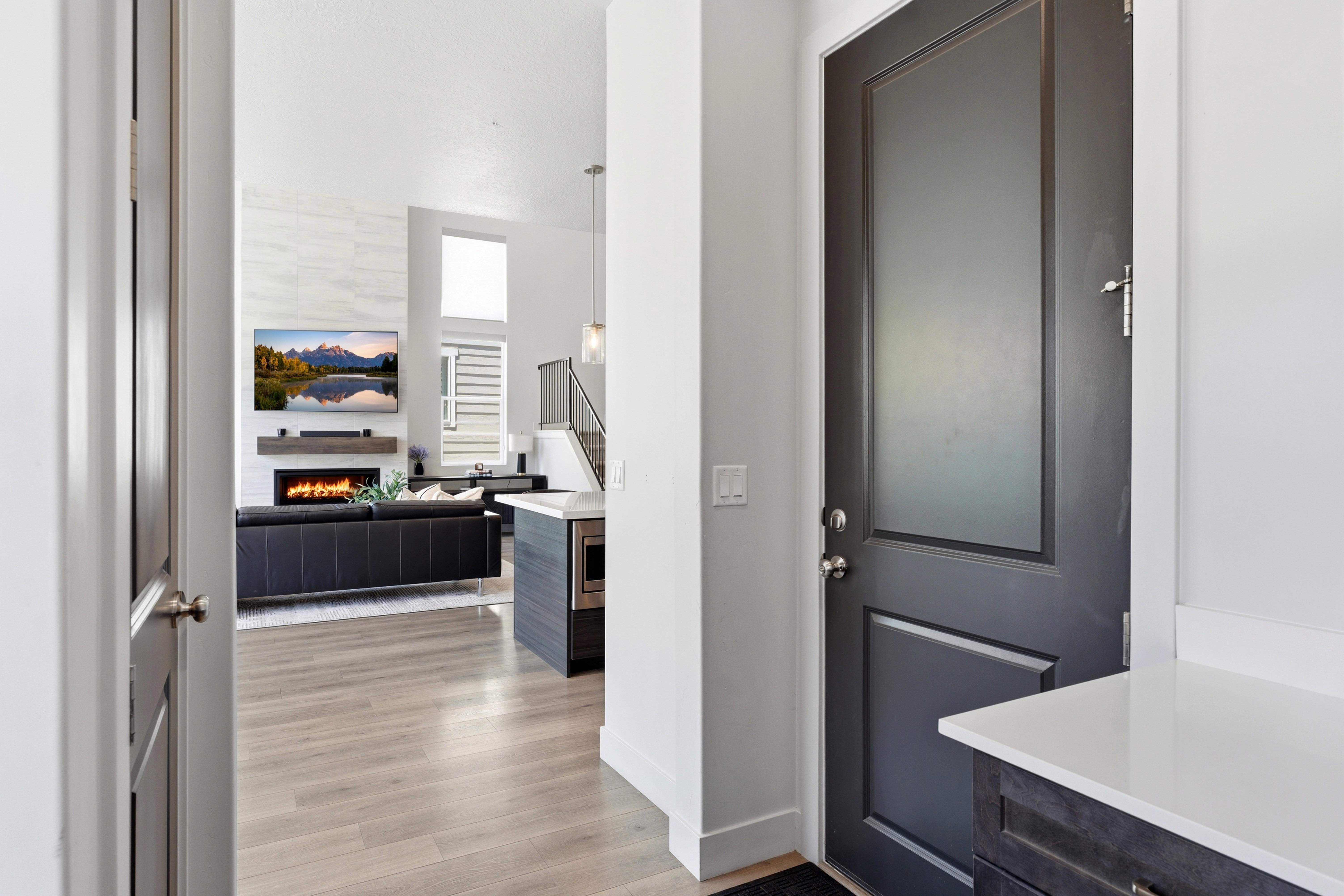 Inviting entry showcasing a dark paneled door, light LVP-finish flooring, a contemporary fireplace with a wood mantel, and an integrated kitchen island with a quartz countertop