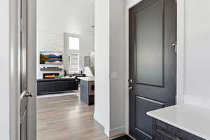 Inviting entry showcasing a dark paneled door, light LVP-finish flooring, a contemporary fireplace with a wood mantel, and an integrated kitchen island with a quartz countertop