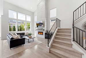 Living room featuring a two-story ceiling, a fireplace with a light-toned tile surround, and multiple tall windows