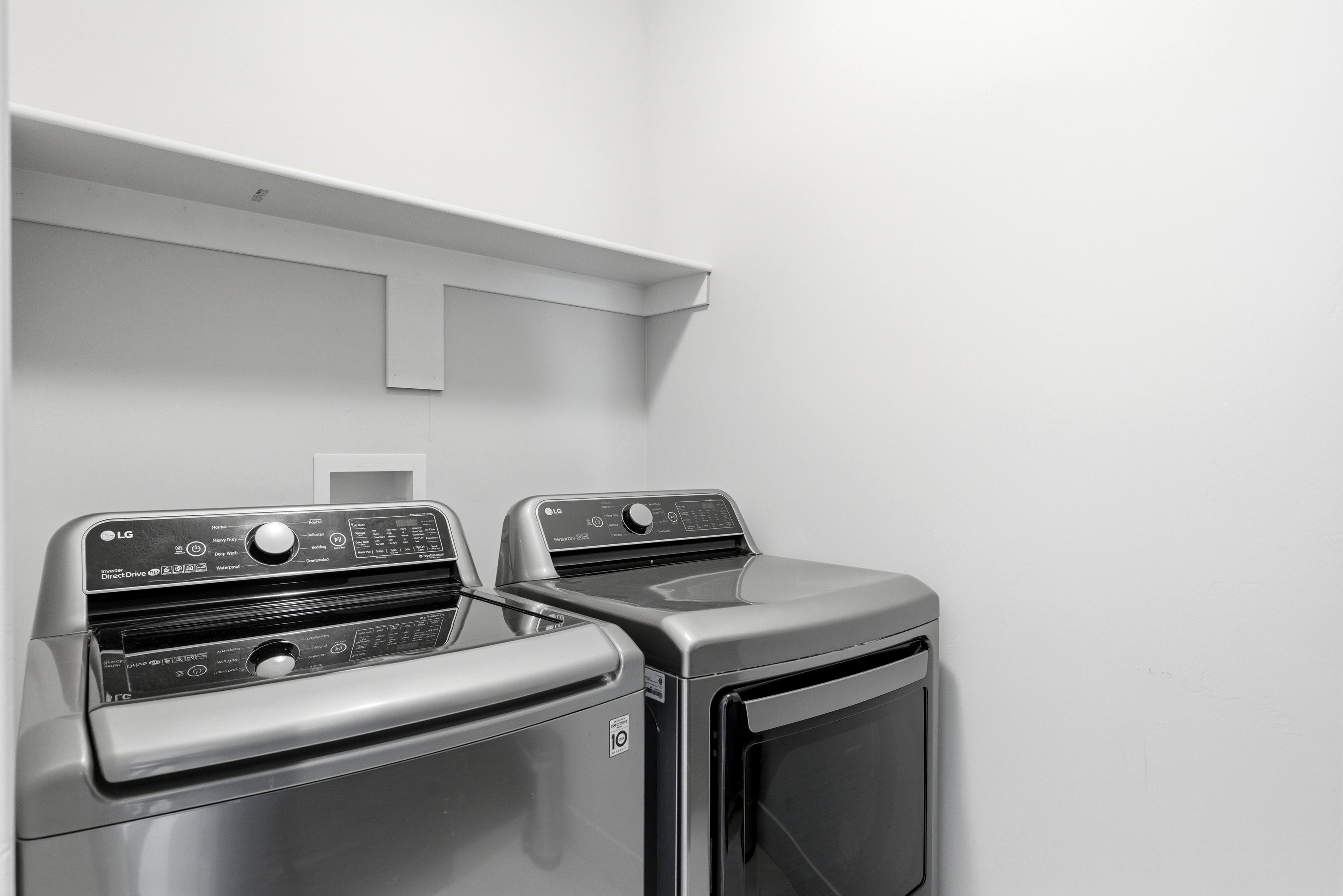 Dedicated laundry space with light gray walls and a built-in white shelf