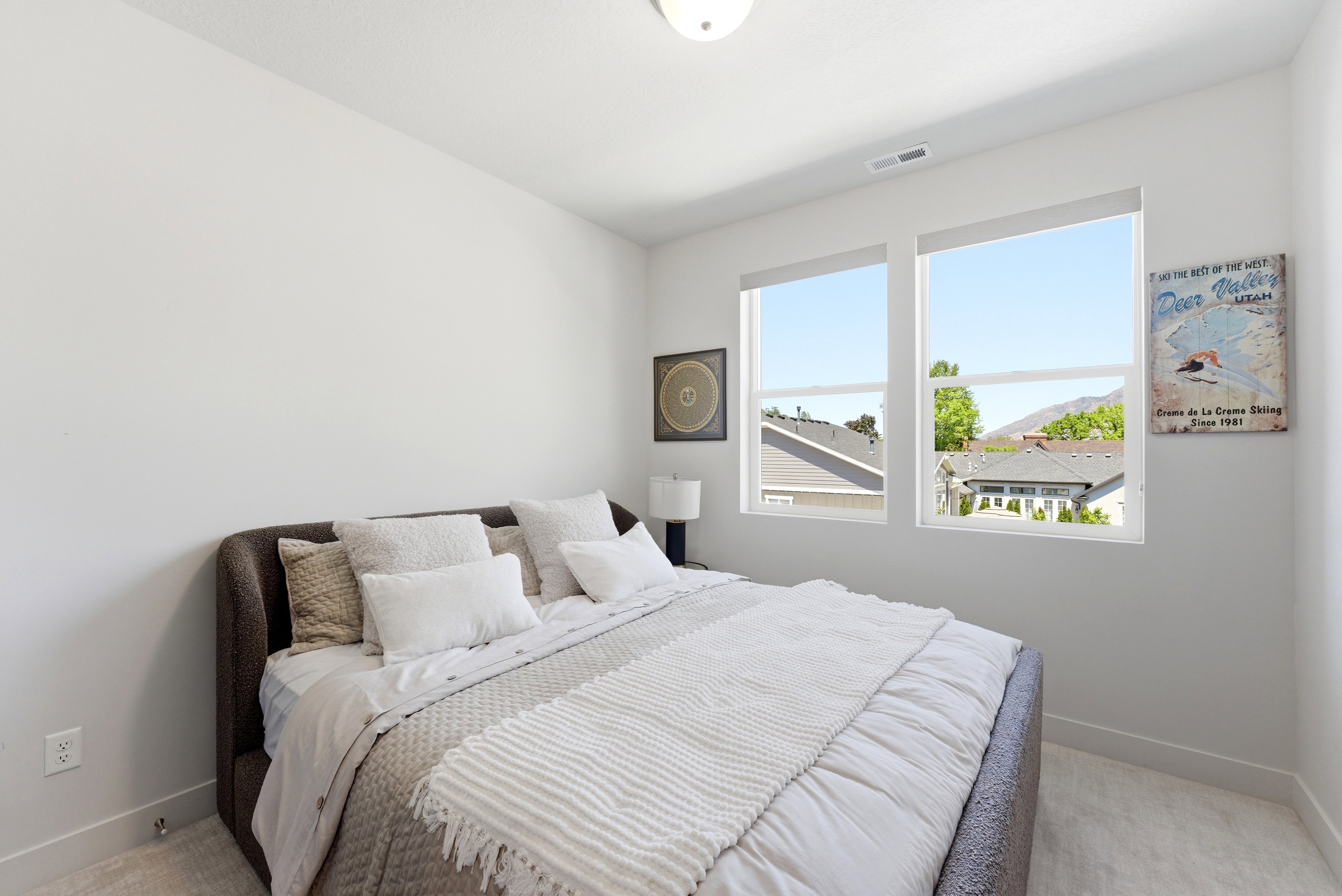 Bright bedroom featuring two large windows, neutral wall tones, and light-toned flooring